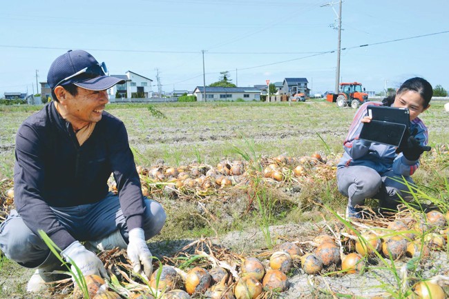 収穫作業中の増田さん（左）を撮影する小林さん（静岡県袋井市で）