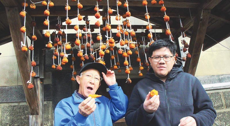 干し柿を食べるバン・グエンさん（右）と山内俊隆さん（秋田県大館市で）