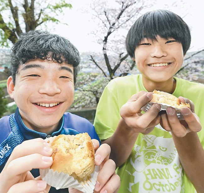 桜のカップケーキを手にした生徒に笑顔が咲いた。背後の桜はソメイヨシノ（神奈川県秦野市で）
