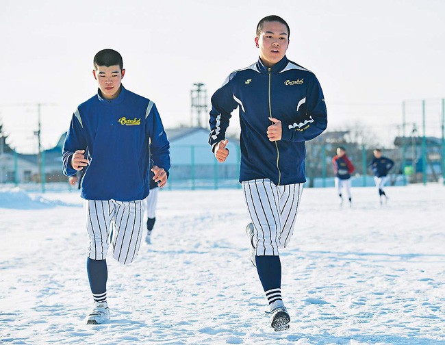 雪が積もったグラウンドの上をダッシュする林選手（右）ら別海高校ナイン（北海道別海町で）